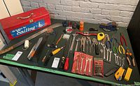 Full view of assorted hand tools spread out on a table including red metal toolbox, pliers, wrenches, screwdrivers, and cutters.