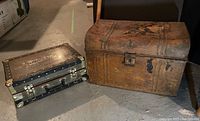 Vintage metal trunk and Mercury Luggage suitcase placed side by side on basement floor, showing size comparison