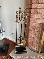 Full fireplace tool set next to brick fireplace with five pieces on stand.