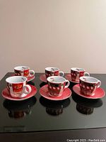 Eight red and white patterned espresso cups on matching saucers arranged in two rows on a black surface.