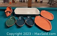 Group photo of all dishes and ceramic figurine on pool table showing different shapes and colors.