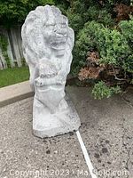 Front view of the concrete lion statue showing face, mane, and paw detail.