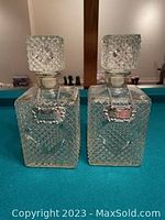 Two vintage crystal glass decanters with stoppers on a green surface, showing textured diamond cut patterns and heavy glass design.