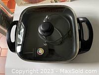 Electric skillet with glass lid on top showing black handles and temperature control cord attached inside skillet.