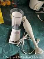Hand blender and beaker on kitchen counter, showing the equipment bundled with power cord, in new condition