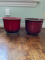 Front view of two red indoor pots placed on a wood-patterned floor against a light blue wall.