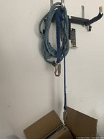 Photo of two hanging ropes, one blue and one grey, each with metal clip attached to one end, hanging on a wall hook.