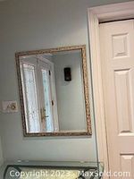 Square framed mirror hung on wall, reflecting nearby door and window.