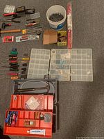 Full overview of the miscellaneous tools including screwdrivers, pliers, hand saw, organizer boxes with small parts, a bucket of screws, and tape roll.