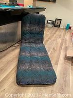 Blue patterned lounge chair cushion folded to show both back and seat sections, placed on wooden floor