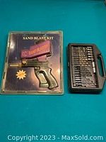The sandblast kit sealed in original plastic packaging alongside a black case holding multiple drill bits.
