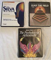 Three audio cassette sets: The Silva Method by Robert B. Stone, Lead the Field by Earl Nightingale, and The Psychology of Achievement by Brian Tracy, shown on a beige fabric background.