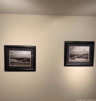 Photo showing two black and white framed landscape art prints hanging on a light-colored wall, both approximately 23"W x 19"H.