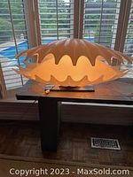 Lamp illuminated on wooden table in front of window, showing scalloped shade glowing warmly