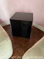 Front angle view of the black glass lacquer side table showing its cube shape and brass corner strips.