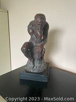 Front view of vintage The Thinker statue showing seated figure in a thinking pose on black base