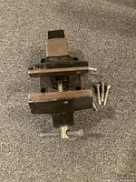 Top view of woodworking bench vice showing wooden jaw plates, screw mechanism, and mounting bolts on carpeted floor.