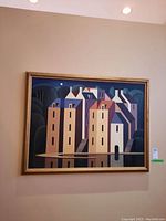 Full frontal view of framed canvas painting showing stylized houses, forest background and water reflection
