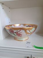 Side view of the large painted decorative bowl showing floral grapes design and gold rim.