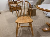 Front view of wooden spindle back chair on carpeted floor with other furniture in background.