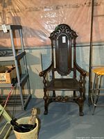 Full view of dark wood framed armchair with ornamental carved top and cane seat/back