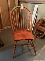 Front view of Windsor-style wooden chair showing curved backrest with vertical spindles, contoured wooden seat, turned legs and stretchers.