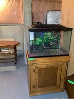 Full view of fish tank on wooden cabinet with visible black hood and decorative plants.