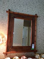 Mirror hanging on a patterned wallpaper background, showing the wood frame with wicker details and bamboo style construction.