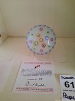 Paperweight showing clear glass with scattered coloured and silhouette floral canes over white latticino ground, certificate in front.