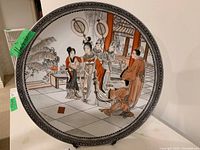 Front view of the decorative bowl-shaped plate showing the full Asian art scene and the patterned border.