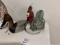 Photo of ceramic rooster container with colorful feather detail next to signed wooden duck decoy