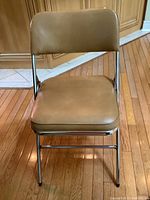 Front view of a single tan vinyl upholstered chrome folding chair showing seat, backrest, and legs