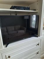 Samsung 32-inch TV model UN32M4500BF sitting on white cabinetry under built-in shelving, visible reflection on screen.