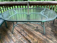 Full view of the oval patio table showing tempered glass top and metal frame structure on wooden deck.