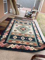 Southwest style area rug spread out on a patio floor showing overall geometric design with diamond shapes and multiple borders in various earth tones.