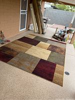 Full view of the area rug laid on a patio floor showing its patchwork pattern and color variety