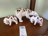 Three white bear figurines displayed on wood surface with MaxSold lot tag. Adult bear and two smaller cubs in white with black and brown tribal geometric patterns.