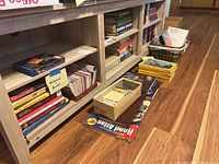 Bottom two shelves filled with books labeled religious books and other genres, boxes and baskets with greeting cards, maps and magazines on floor