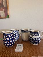 Four ceramic pitchers on wooden table, displaying all four distinct designs and overall size.