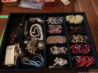 Photo of assorted costume necklace and pins organized in a black tray with multiple compartments