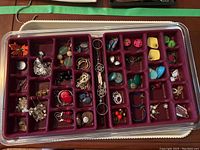 Photo showing one jewelry tray filled with assorted costume jewelry pieces including earrings, rings, necklaces, and pendants organized by compartment.