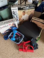 Full lot comprising back massager box, FlexaBall exercise ball box, various hand weights, ankle weights, and resistance bands arranged on the floor.