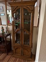 Full view of the tall wood hutch cabinet showing its finish, glass doors, and lower storage compartment.