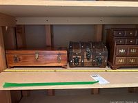 Two wooden jewelry boxes on shelf, one cedar rectangular box and one small trunk style box with metal decoration.