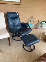 Black leather reclining swivel chair with matching ottoman shown angled beside beige chairs and wall decorations.
