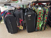 Four suitcases upright: a large colorful ladybug pattern, two medium black suitcases, and one smaller black Dockers carry-on suitcase.