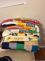 Stack of three colorful handmade quilts in various patchwork patterns and colors.