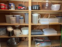 Four shelves of assorted Tupperware containers, white pitcher, butter dishes, mugs, and kitchen items.