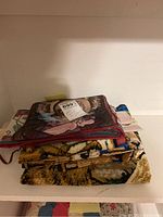 Stack of folded vintage tapestries and textiles on a shelf.