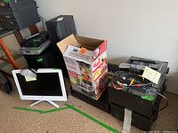 Photo showing Windows 10 all-in-one monitor with white frame, various stereo components stacked, box for kitchen appliance partially visible in background.